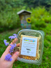 Load image into Gallery viewer, Wild Indigo Forest Farm raw comb honey package held beside purple flowers at Diagon Apiary